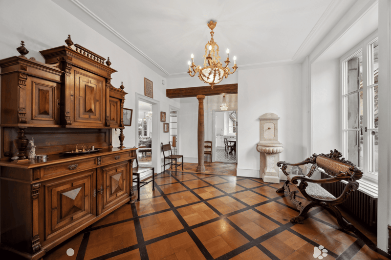 elaborate wooden furniture, hardwood floor with black trim, chandelier, wooden bench, radiator, windows