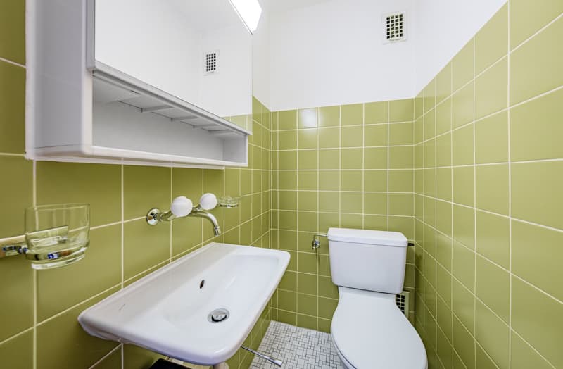 Bathroom with green tiles, white sink, white toilet, glass cup holder, silver faucet
