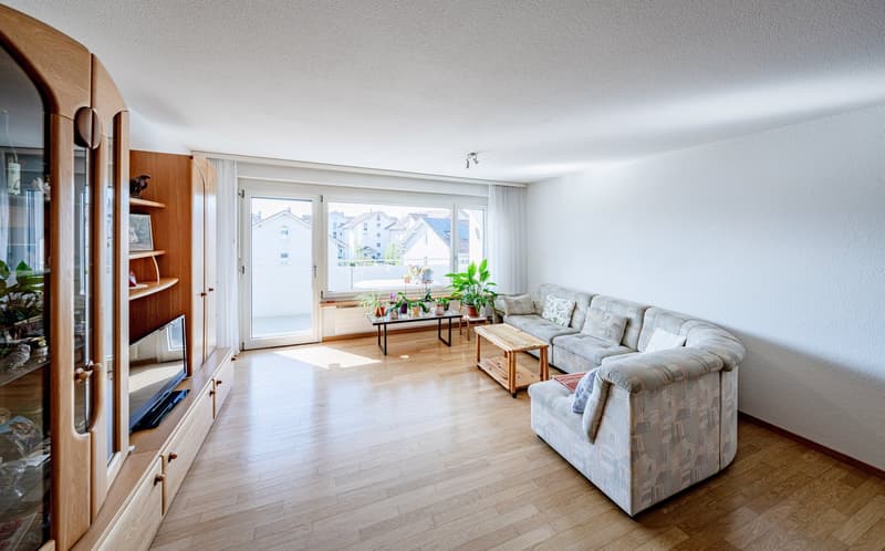 living room with wooden floor, white walls, large windows, balcony, couch, coffee table, TV cabinet, plants
