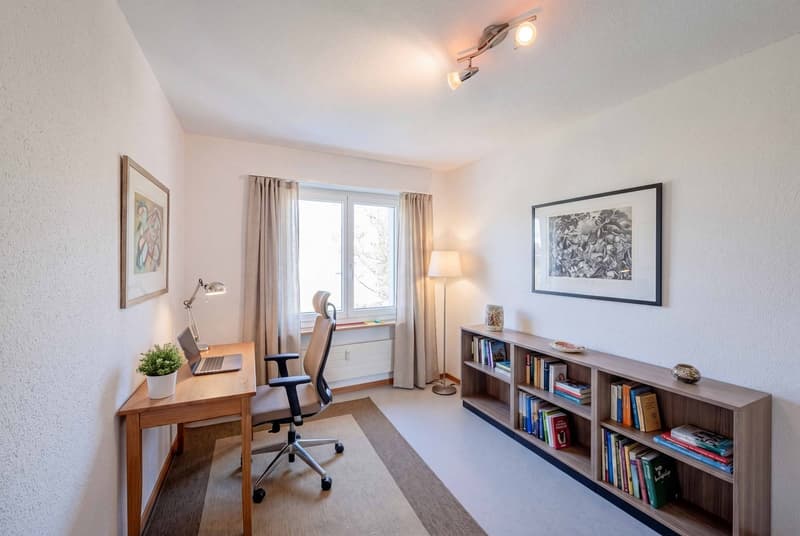 A room with a desk, office chair, lamp, books, and a window with curtains.