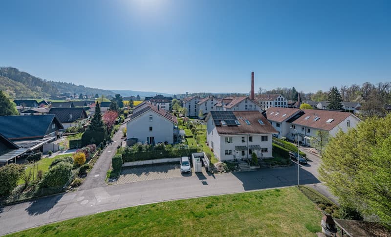 Aerial view of a residential area with several houses, solar panels, and a driveway.
