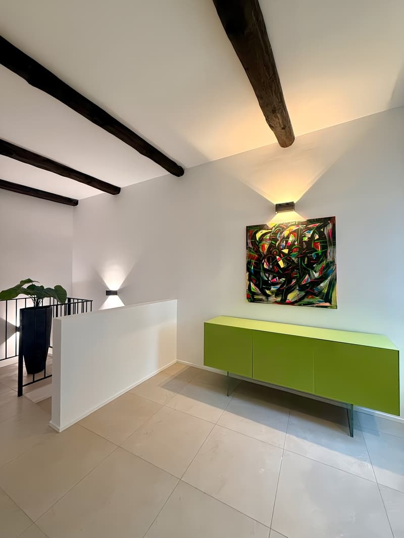 white walls, wooden ceiling beams, green cabinet, potted plant, painting, light fixtures, tiled floor, balcony with railing