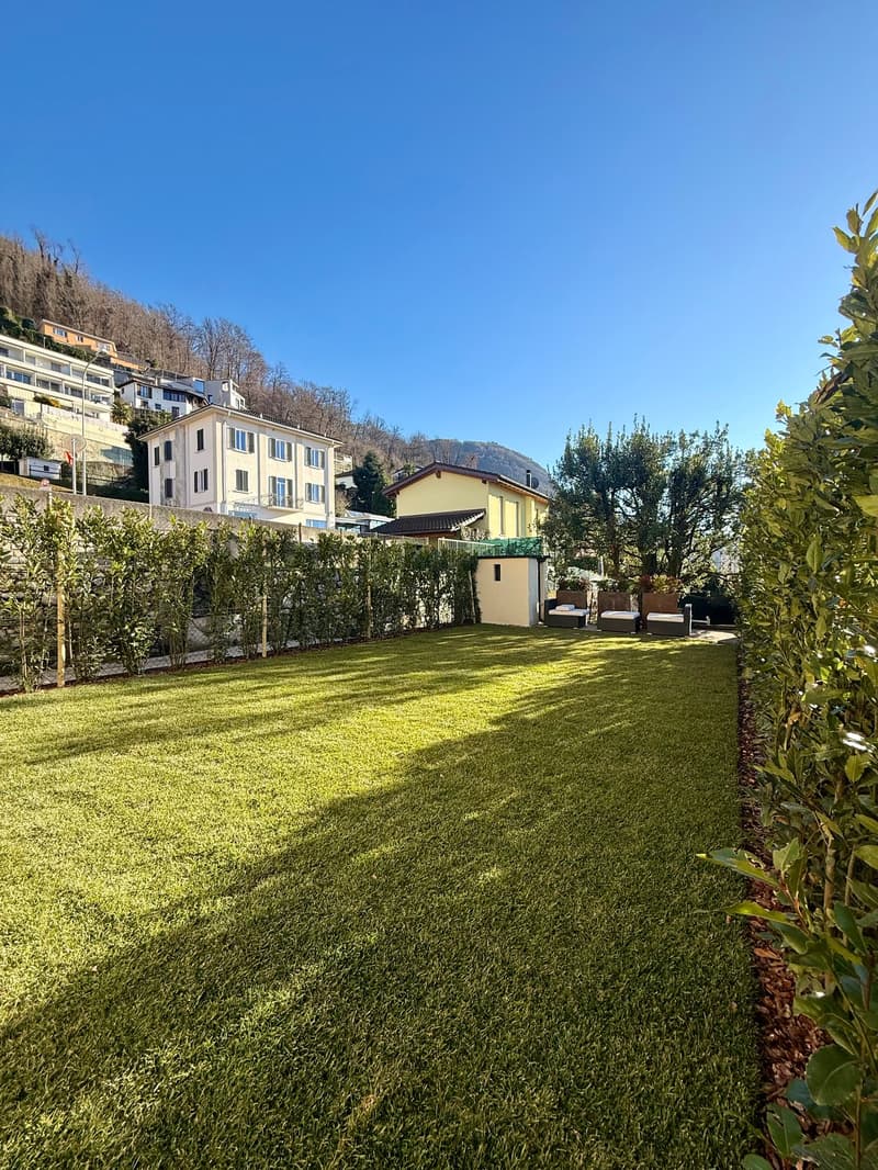 Well-manicured lawn, greenery, outdoor seating area, buildings in the background, and a view of the hills