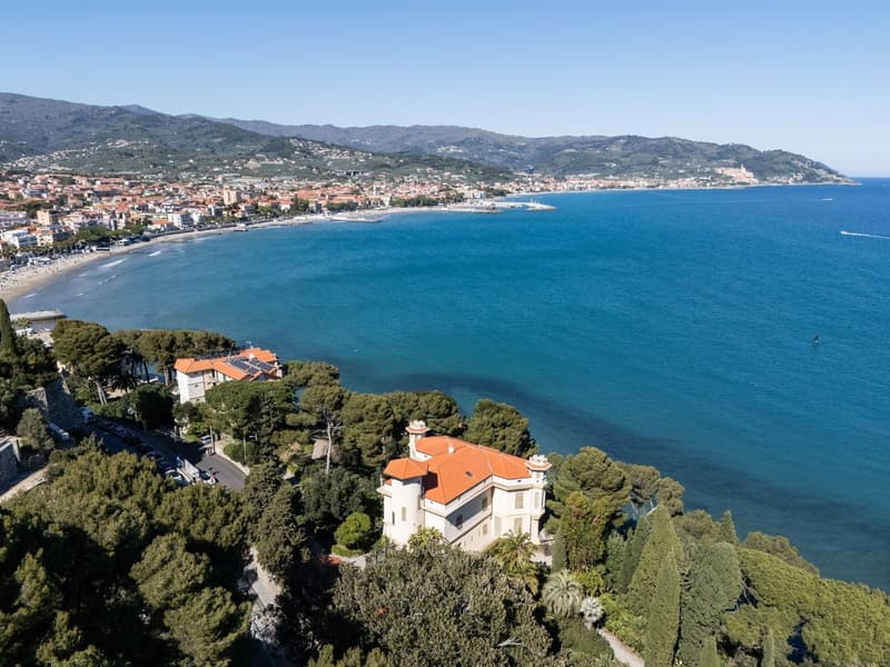 Villa with orange roof, surrounded by trees, overlooking the sea and a town