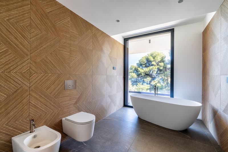 modern bathroom with wooden wall, white bathtub, white toilet, white sink, glass window
