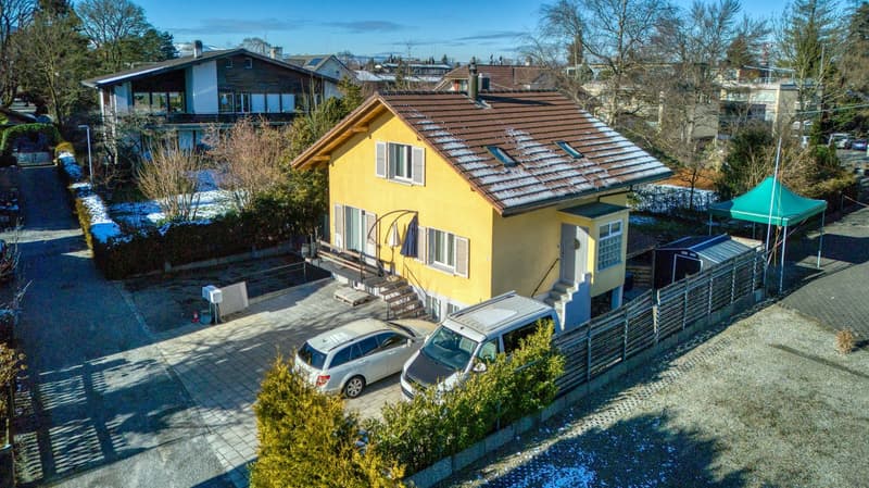 two story yellow house with brown roof, 2 cars parked, fence, 3 windows, garage