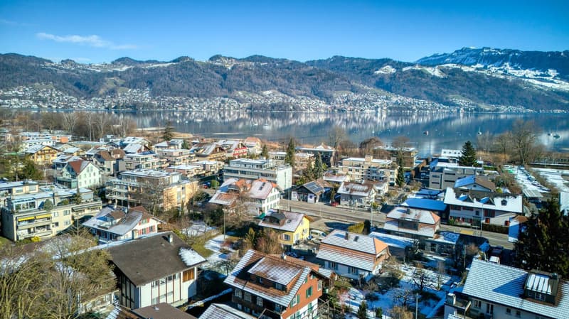 Snow-covered rooftops, urban area with houses, snowy mountains, winter scenery, large lake with reflection