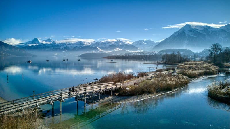 lake with mountains, small wooden bridge over the water, a couple sitting, snowy mountains in the background