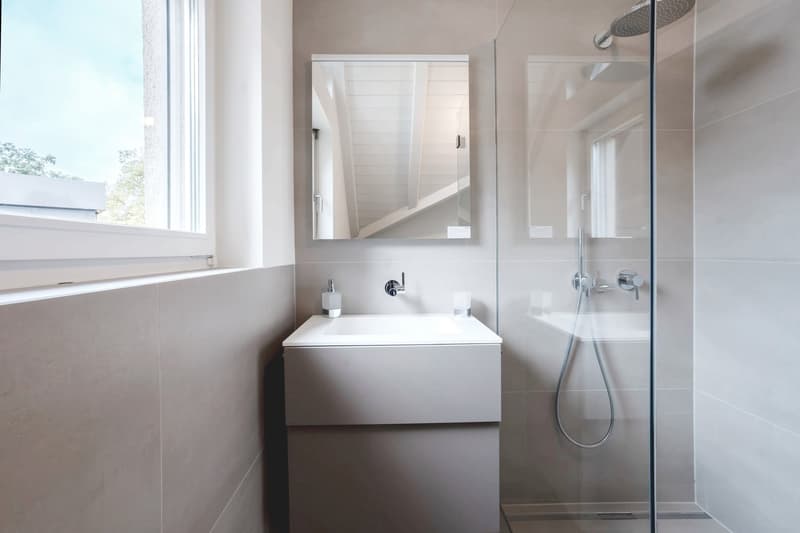 modern bathroom with white tiles, a glass shower, a vanity with sink, a mirror, and natural light from a window