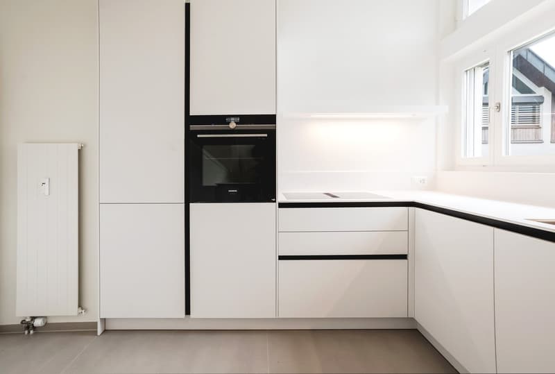 Modern, fully equipped kitchen with white cabinets, black stove, integrated dishwasher, and private washing machine.