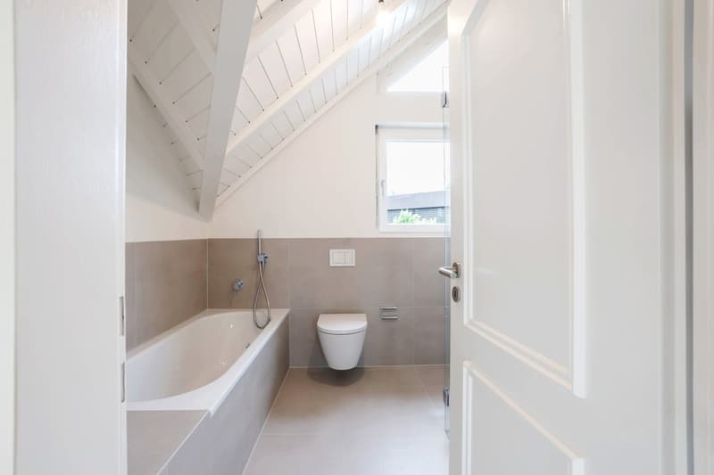 minimalist bathroom with bathtub, toilet, and a small window, white and gray tiled walls