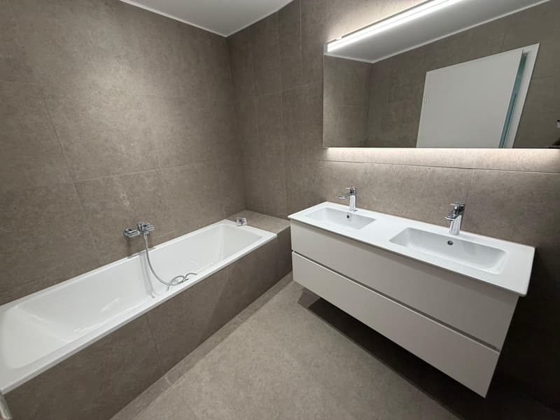 modern bathroom with bathtub, double sink, mirror, and tiled walls