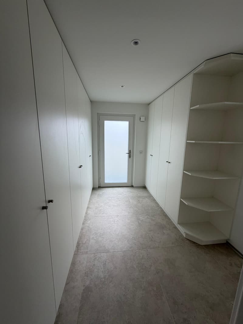 Empty hallway with white walls, tiled floor, and built-in cabinets on both sides.
