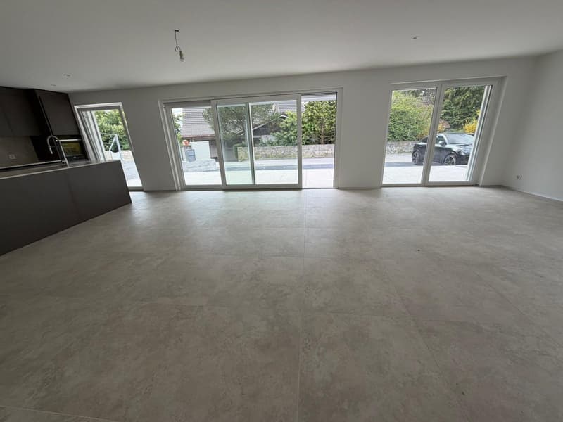 Empty room with large windows, tiled floor, kitchen area with sink and faucet