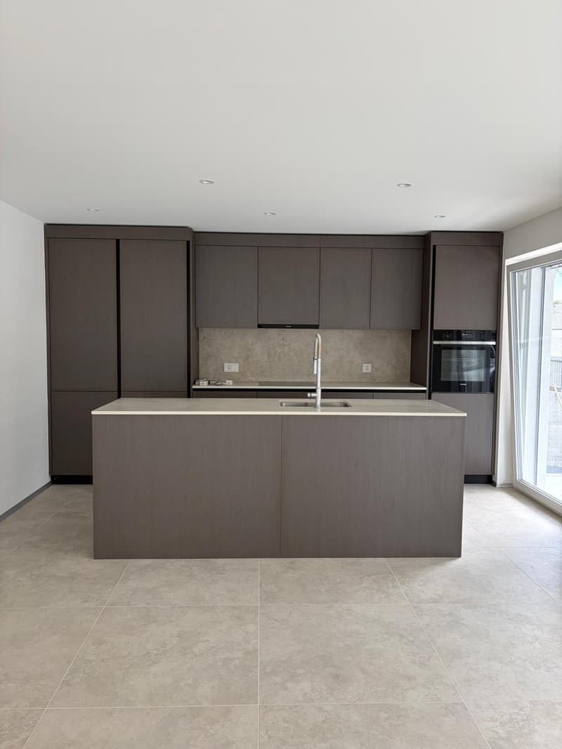 modern kitchen with island, dark cabinets, tiled floor, large sink, stainless steel faucet, built-in oven, sliding glass door