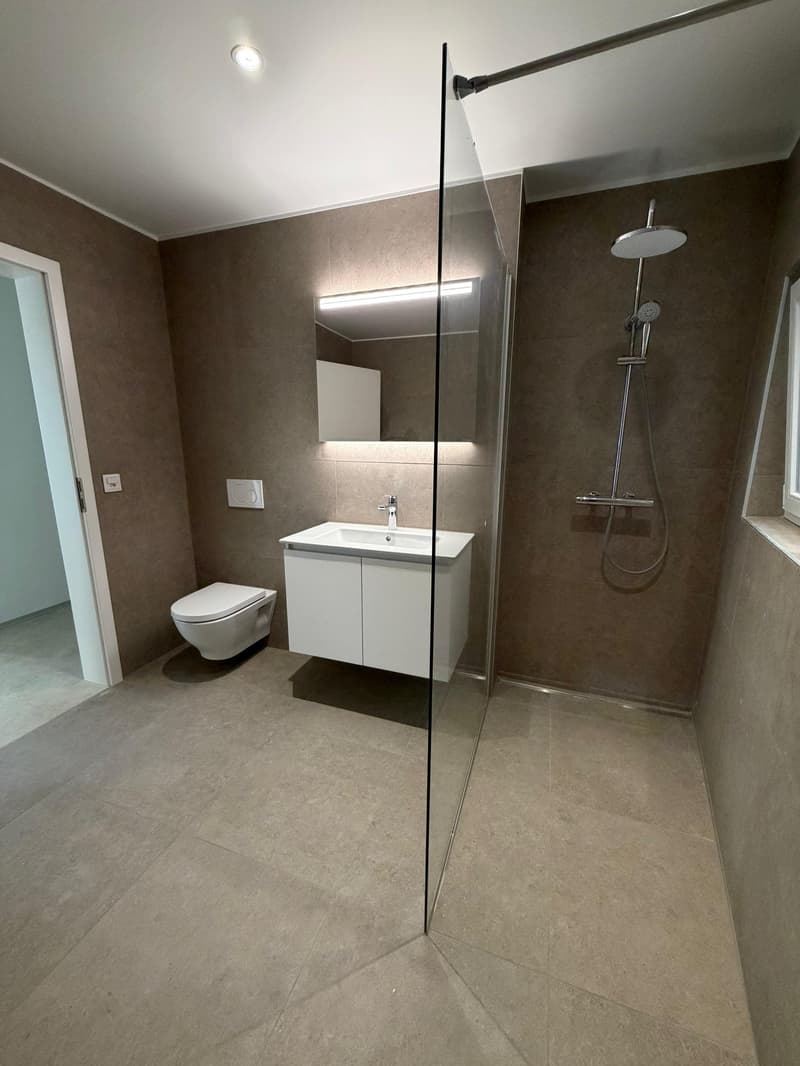 modern bathroom with white sink, glass shower enclosure, white toilet, mirror, and beige tiles