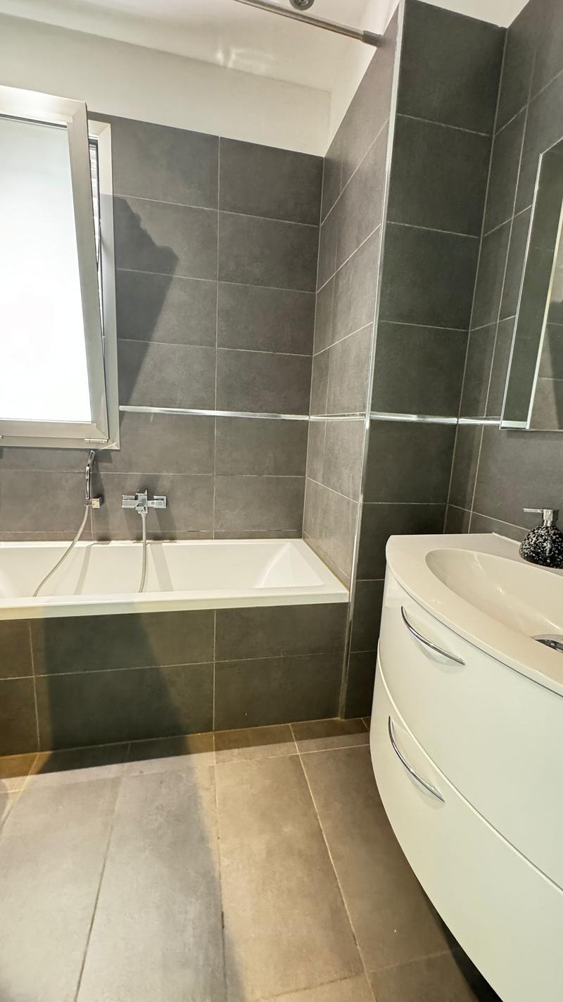 Modern bathroom with a bathtub, sink, gray tile walls, and tiled floor.
