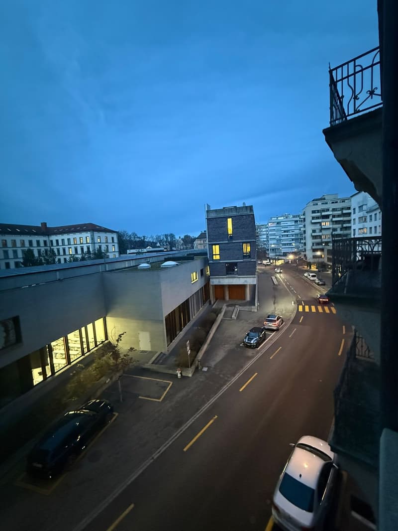 City street with cars, buildings, night view, balcony visible in the frame.