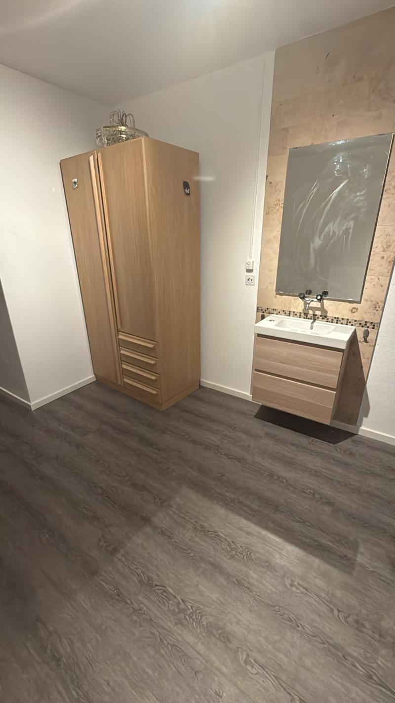 Bathroom with white wall, brown floor, mirror, sink, wooden cabinet, large cupboard, and a power outlet.