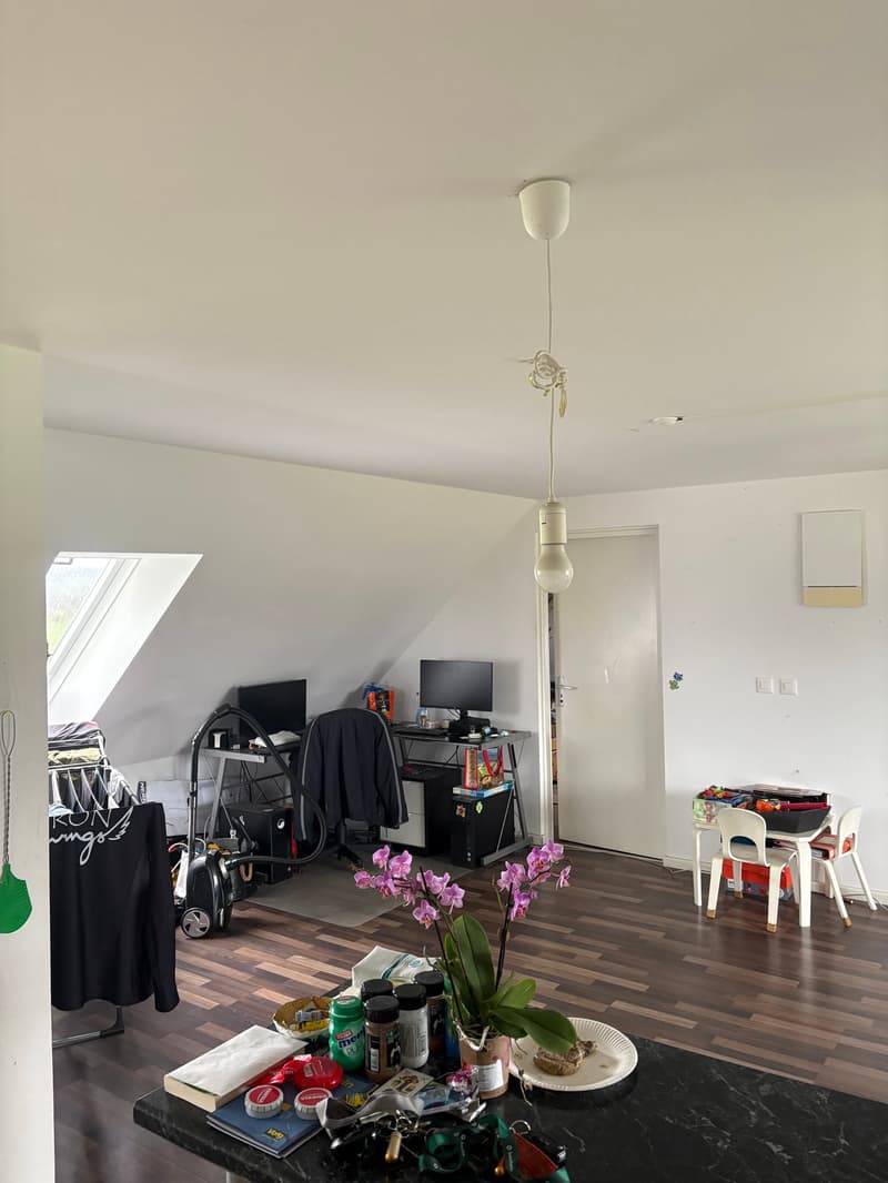 attic room with wooden floor, desk with computer and chair, hanging lamps, small flower on desk, small table, and chair