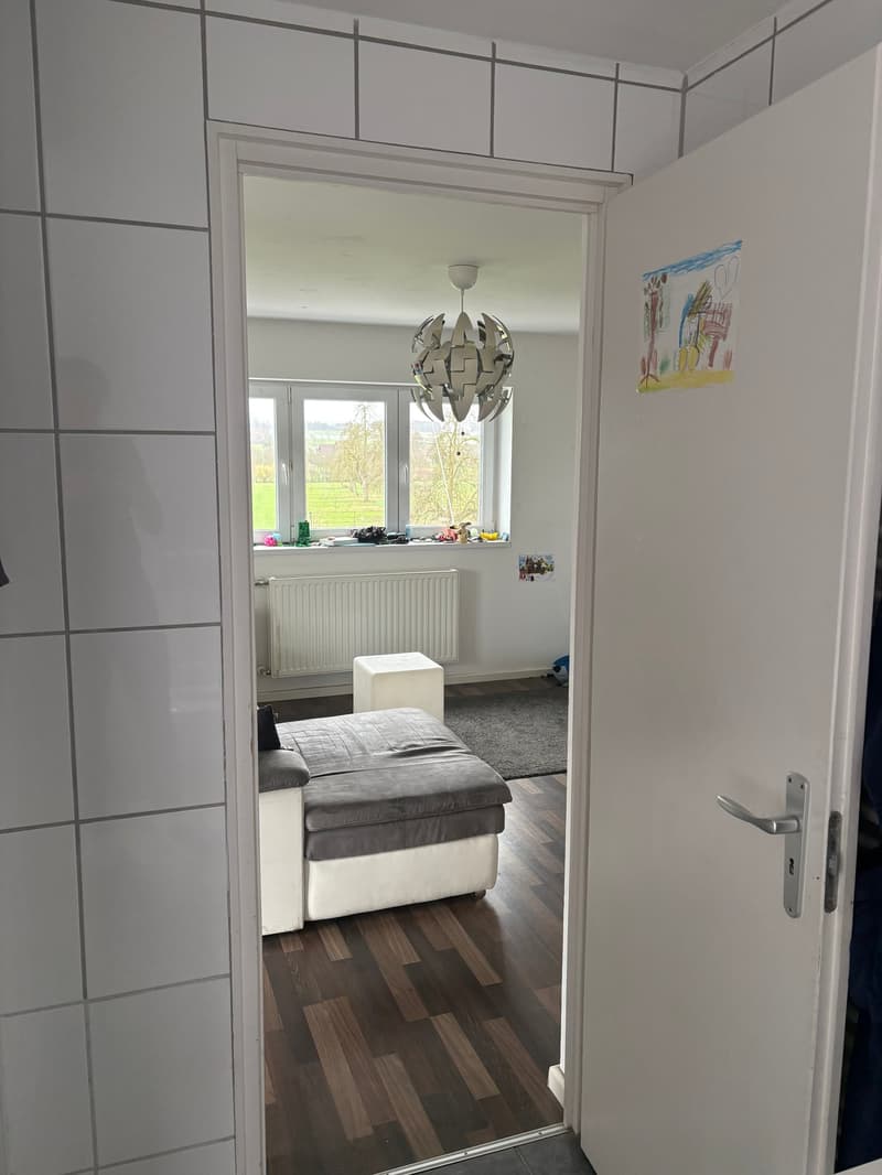 Bedroom with white walls, wooden floor, double bed, radiator, and window with a view.