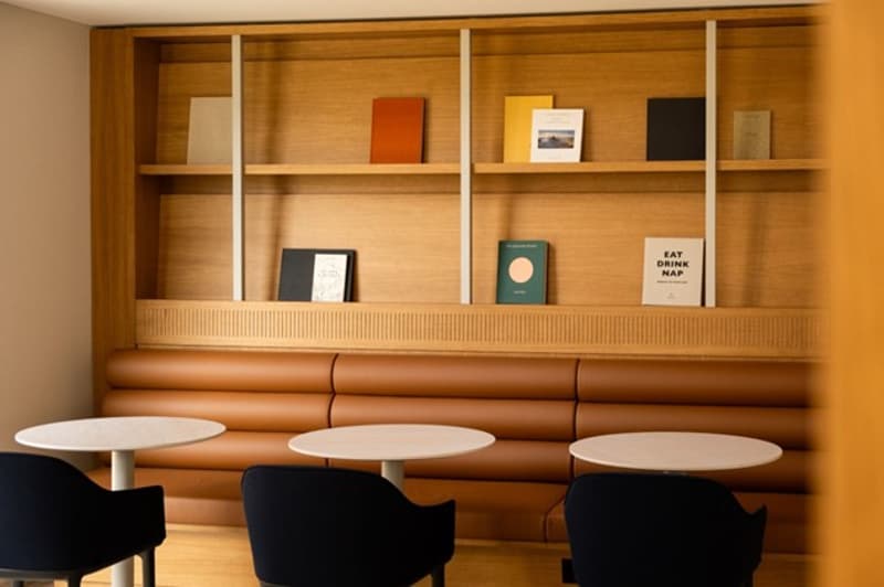 Interior of a room with wooden shelves, round tables, and chairs. The room has a contemporary and minimalistic design, with wooden and black furniture.