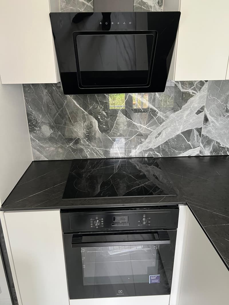 modern kitchen with black marble countertops, black induction stove, black microwave, black oven, white cabinets