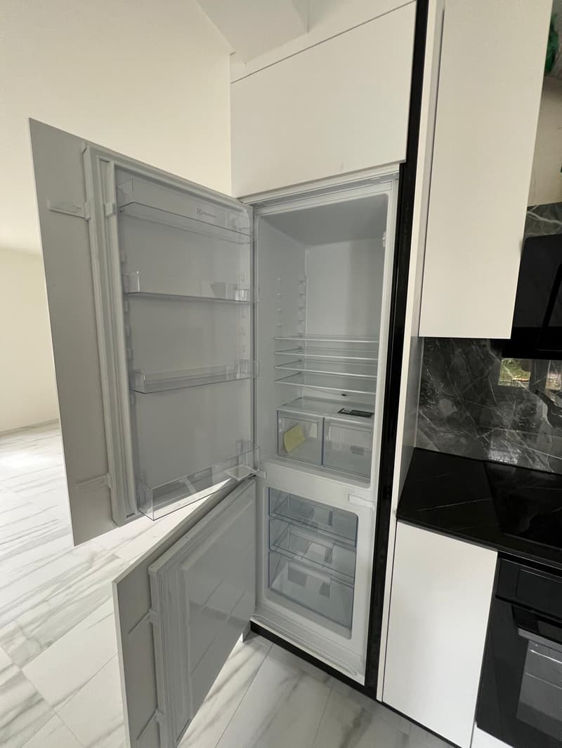 Open refrigerator with glass shelves, drawers, and compartments, white cabinets, marble floor, black countertop, oven