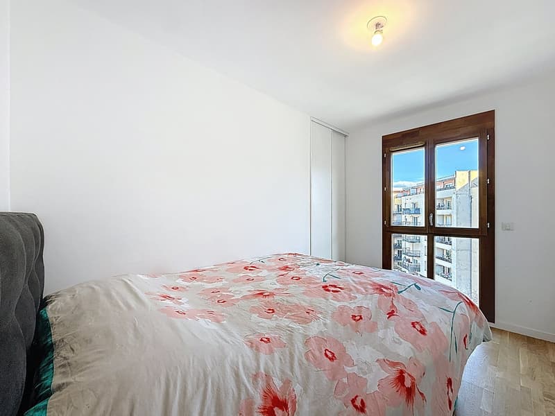 Bedroom with bed, white walls, wooden floor, large window with view of the outside