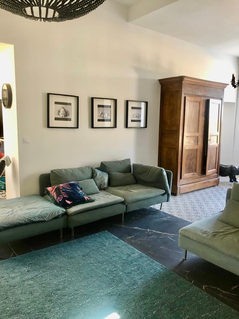 Living room with a green sofa, a wooden cabinet, a chandelier, a rug, and three framed pictures on the wall