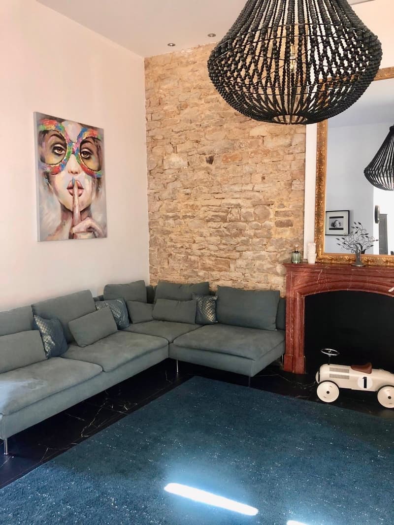 L-shaped sofa, brick wall, fireplace, painting, mirror, chandelier, rug