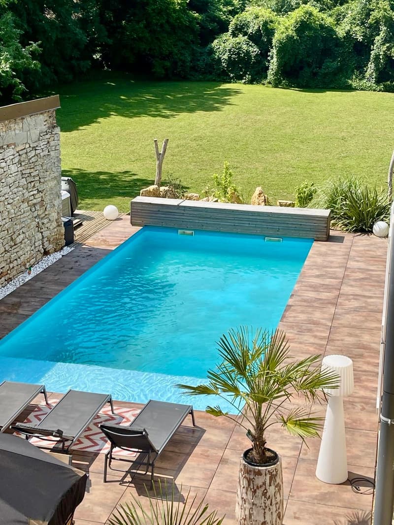 Outdoor swimming pool, wooden deck, lounge chairs, potted plants, grassy lawn, stone wall