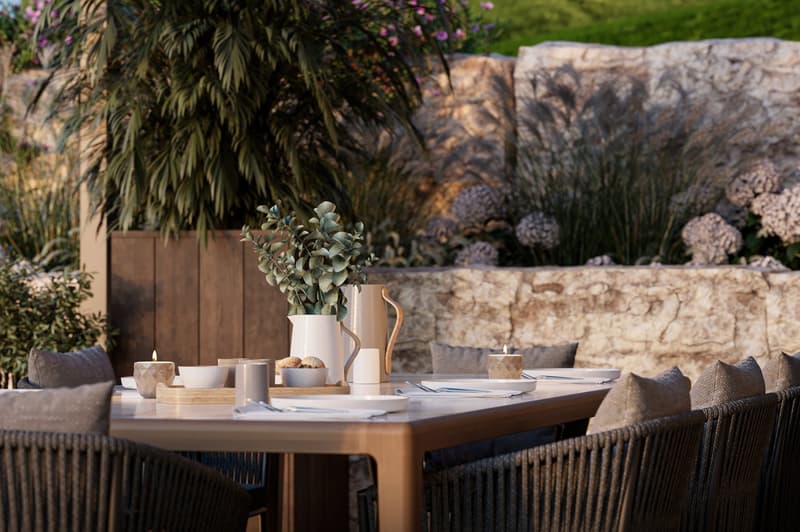 Outdoor dining table with chairs, stone wall background, plants, candles, natural light