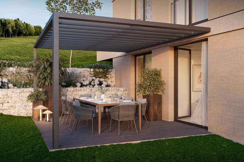 Outdoor dining area with a wooden table, chairs, and a pergola, set against a backdrop of greenery and a grassy lawn, with a view of the landscape