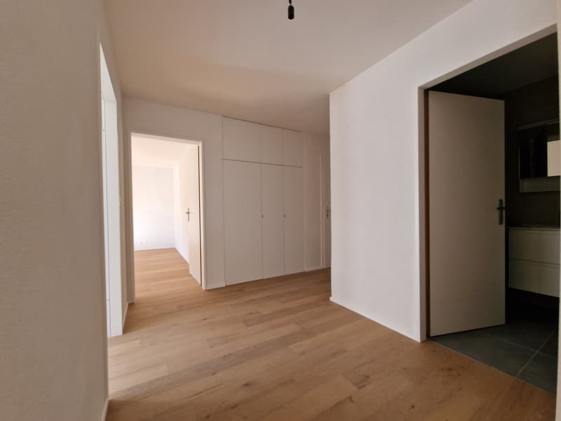 Empty room with wooden floor, white walls, built-in wardrobes, open door leading to another room