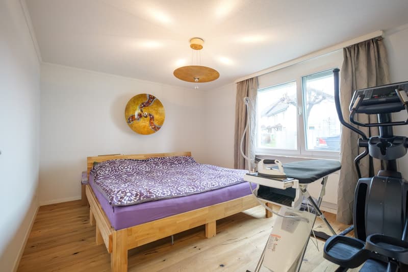 bedroom with a double bed, wooden floor, white walls, a ceiling light, a wall painting, a window, and exercise equipment