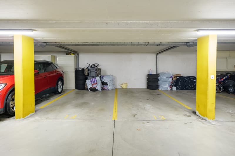 underground parking garage with two cars parked, concrete floor, two yellow lines dividing parking spaces, one parking space without car