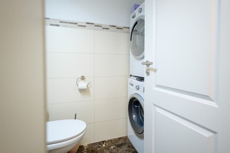 small room, white washing machine, dryer, white toilet, roll of tissue paper
