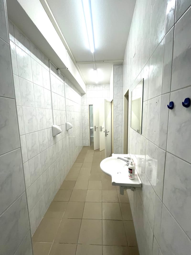 long corridor with tile floor, white tiled walls, sink with mirror, two doors at the end