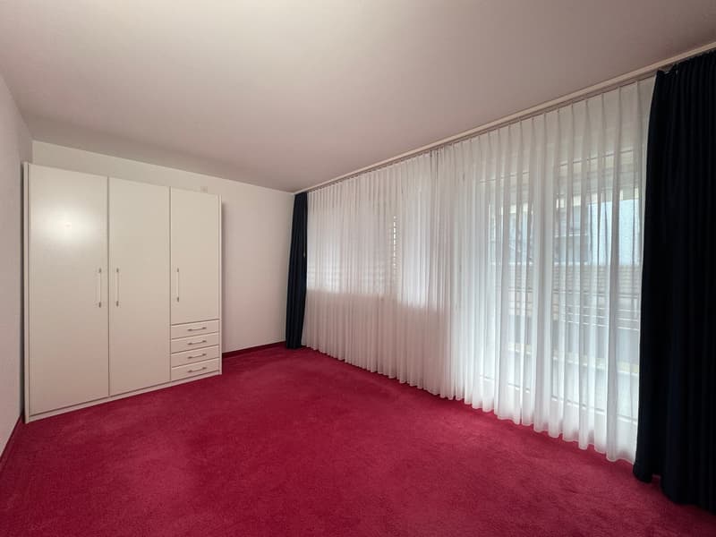 Empty room with white walls, white curtains, red carpet, and white wardrobe.