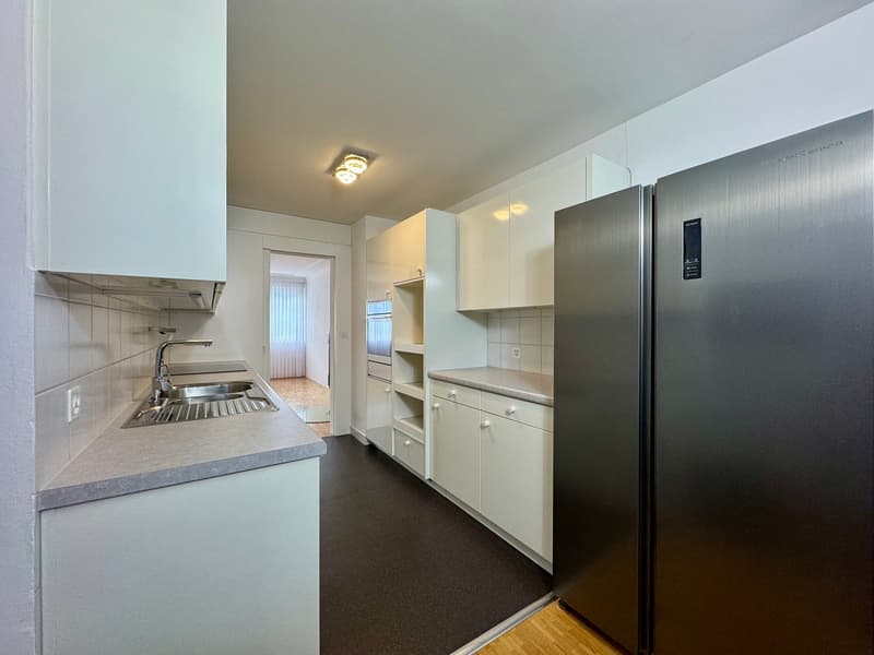 Kitchen with stainless steel refrigerator, sink, tiled countertops, built-in cabinets, tiled backsplash, and ceiling lights.