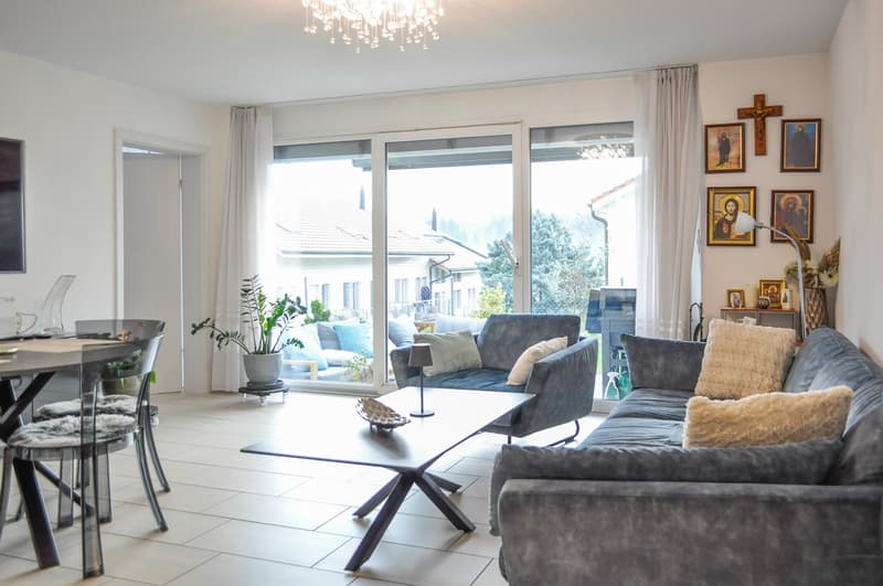 Cozy living room with white walls, gray couches, and wooden coffee table. It includes sliding doors leading to a patio and view to outside landscape.
