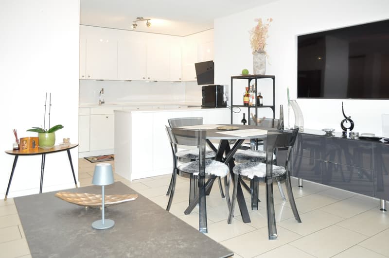 modern living room with dining area, white kitchen, tiled floor, flat screen TV, white cabinets, small dining table, decorative items
