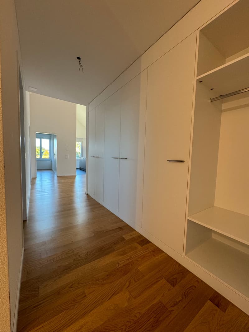 Empty hallway with wooden floor, white walls, and built-in wardrobes