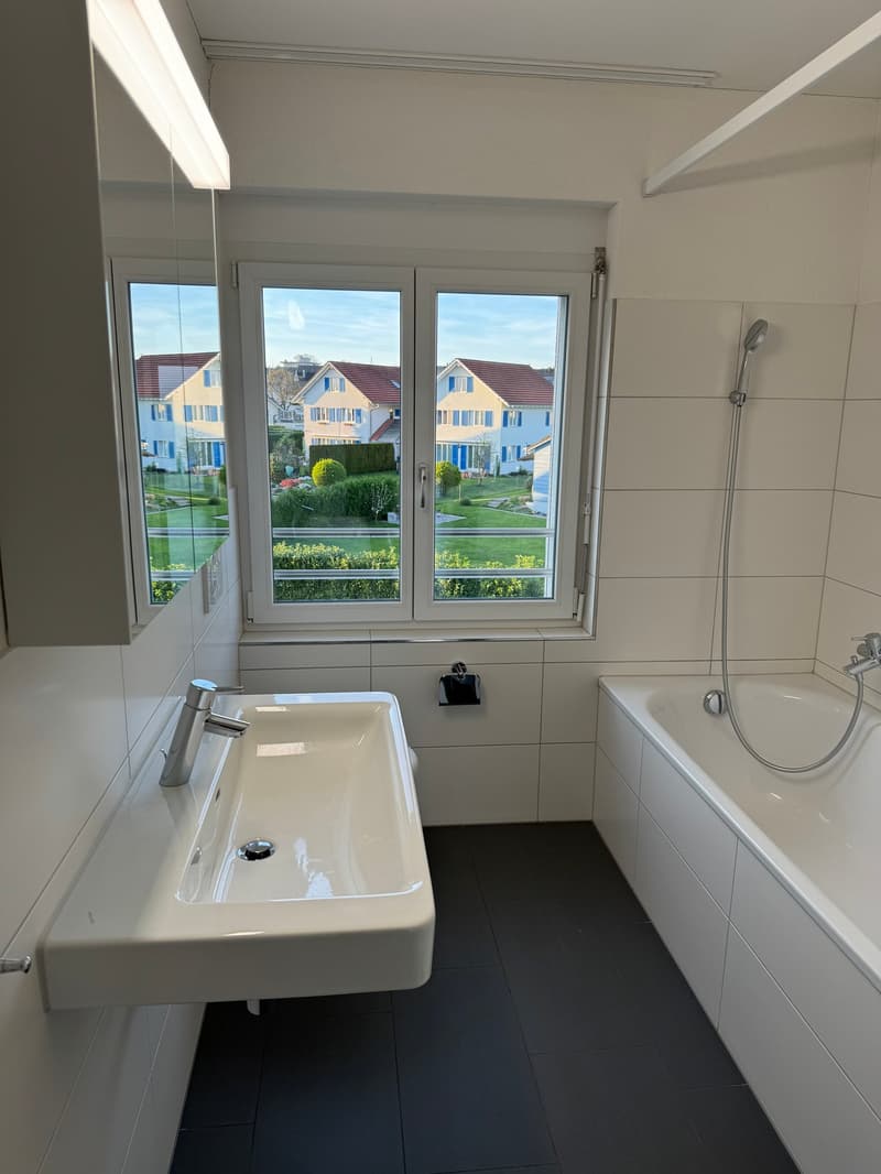 modern bathroom with white tiles, white sink, bathtub, shower, mirror, and window with view