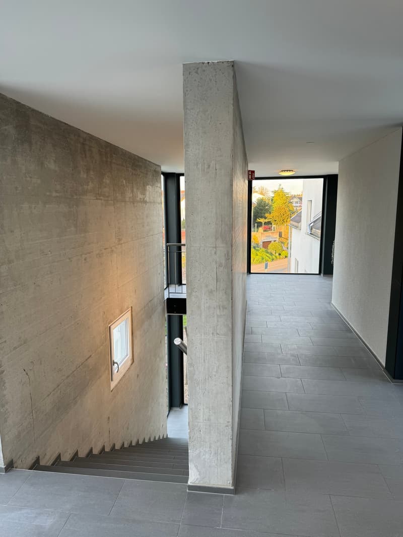 Concrete walls, tiled floor, staircase, small window, balcony with railing, glass door, view of trees and buildings