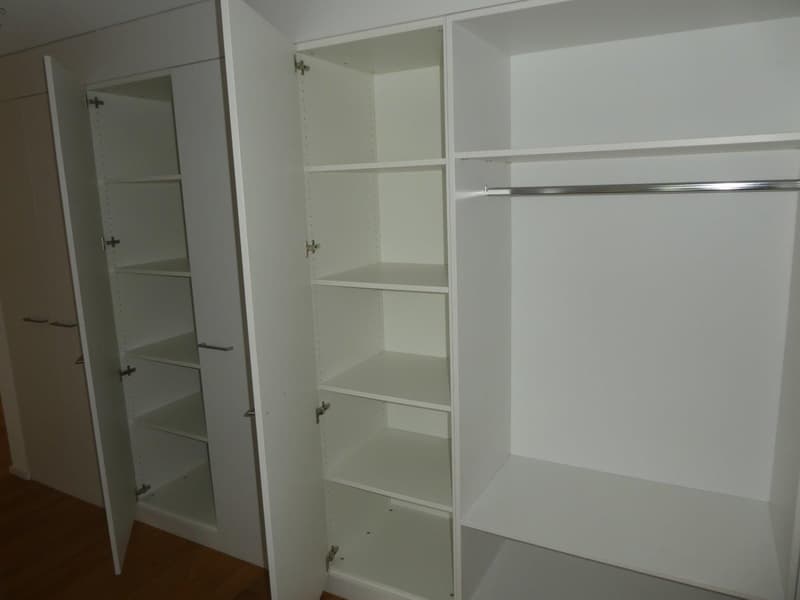 Empty white wardrobe with multiple shelves and a hanging rod