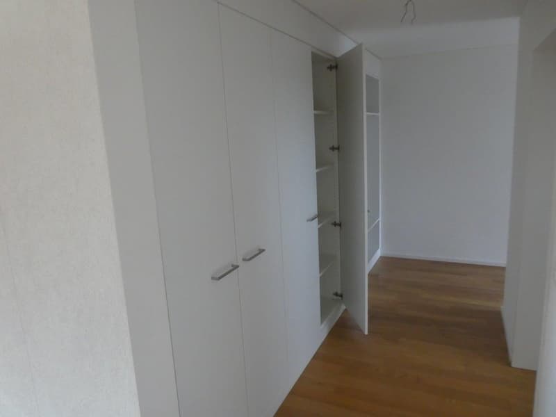 Empty room with white walls, wooden floor, and built-in wardrobes