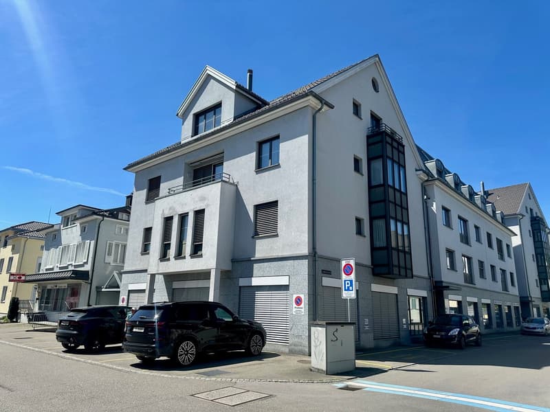 4 story building, grey exterior, multiple windows, garage, multiple cars parked in front