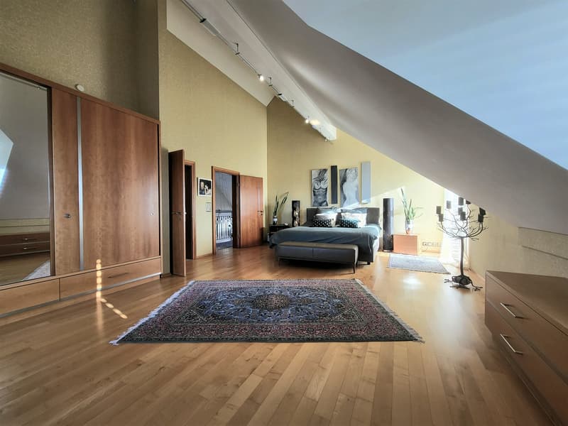 Bedroom with wooden floor, large bed, rug, wooden cabinet, mirror, and plants